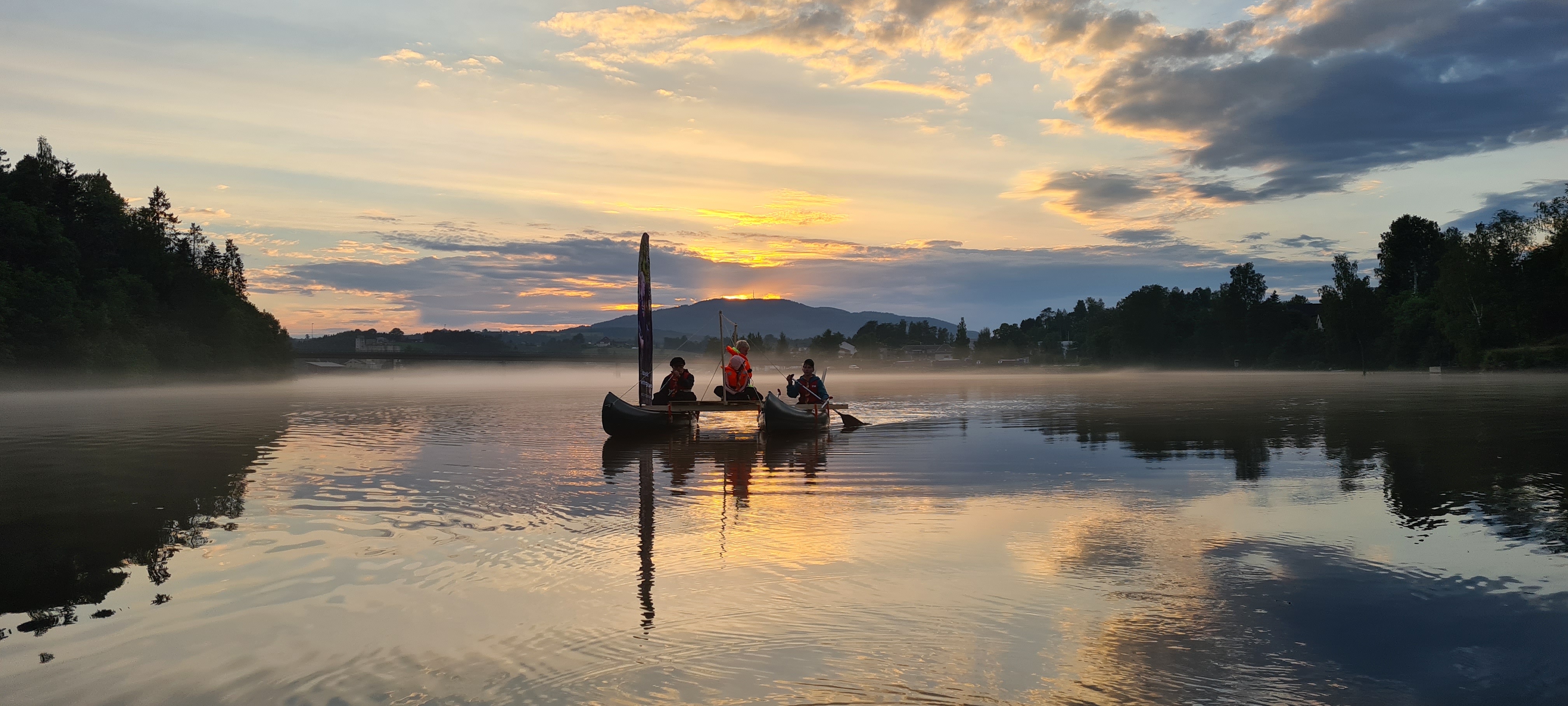 Speidere seiler på en hjemmelaget katamaran av kanoer i solnedgang over stille vann