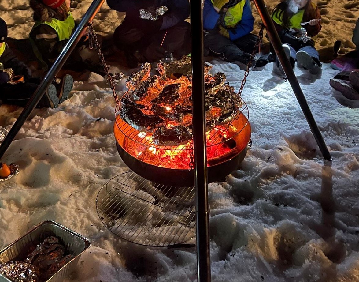 Speidere rundt et bål om vinteren med mat pakket i aluminiumsfolie på en grillrist