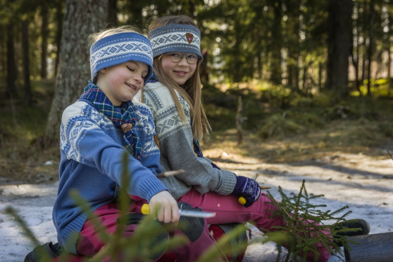 To barn sitter i skogen og spikker med kniv