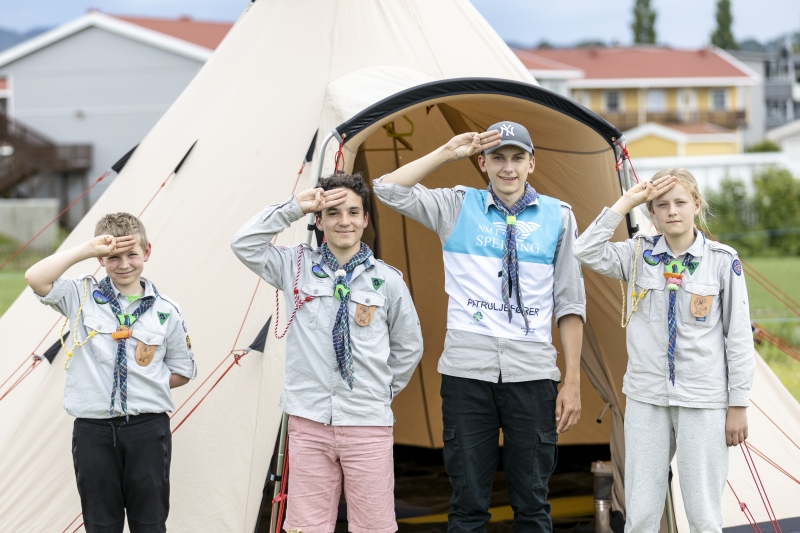 Fire speidere i uniform hilser foran et lavvotelt
