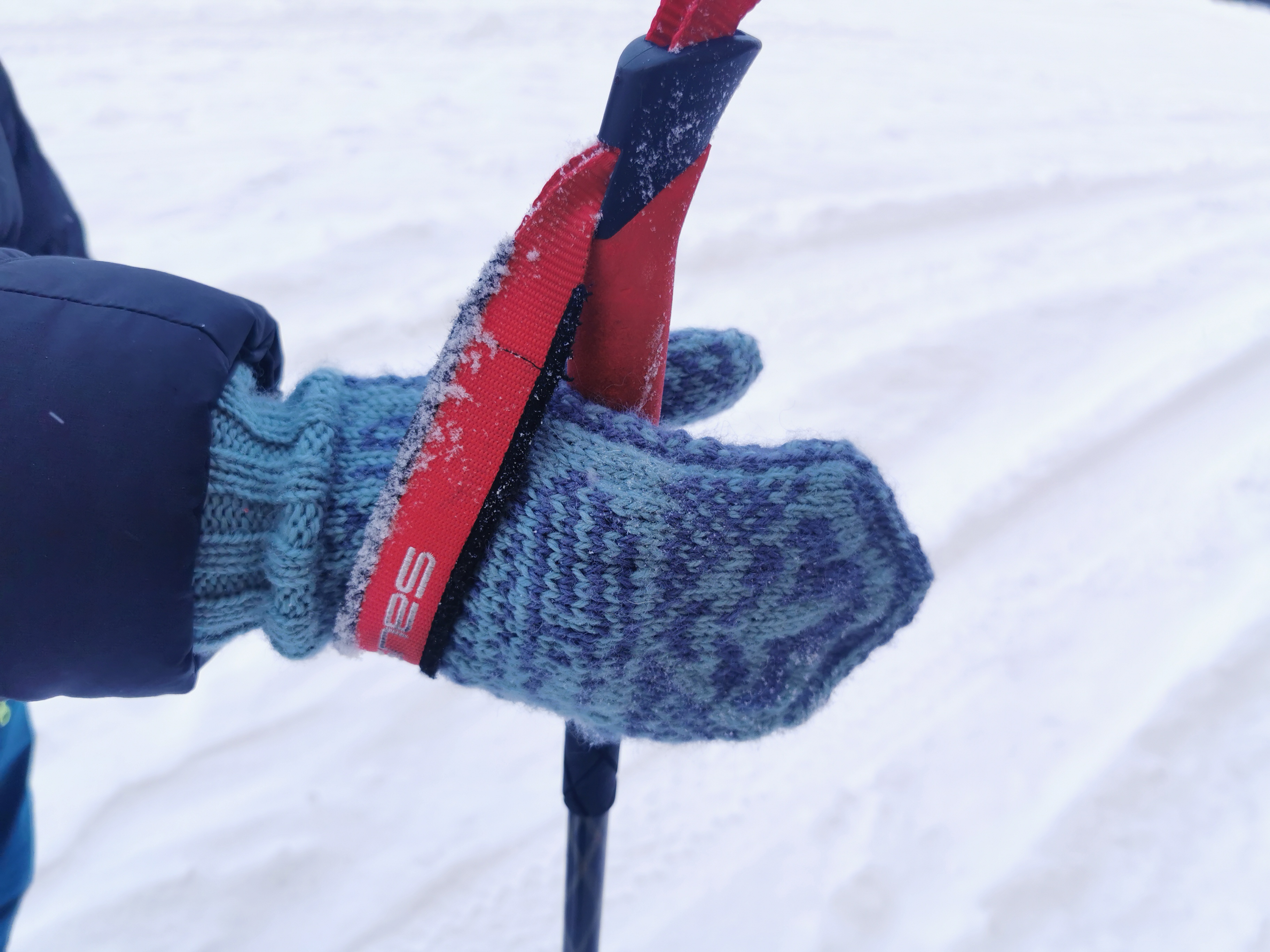 Hånd med hjemmestrikket speidervott holder en skistav i snøen