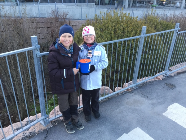 To speidere står sammen og holder i speideraksjons-bøssa og smiler