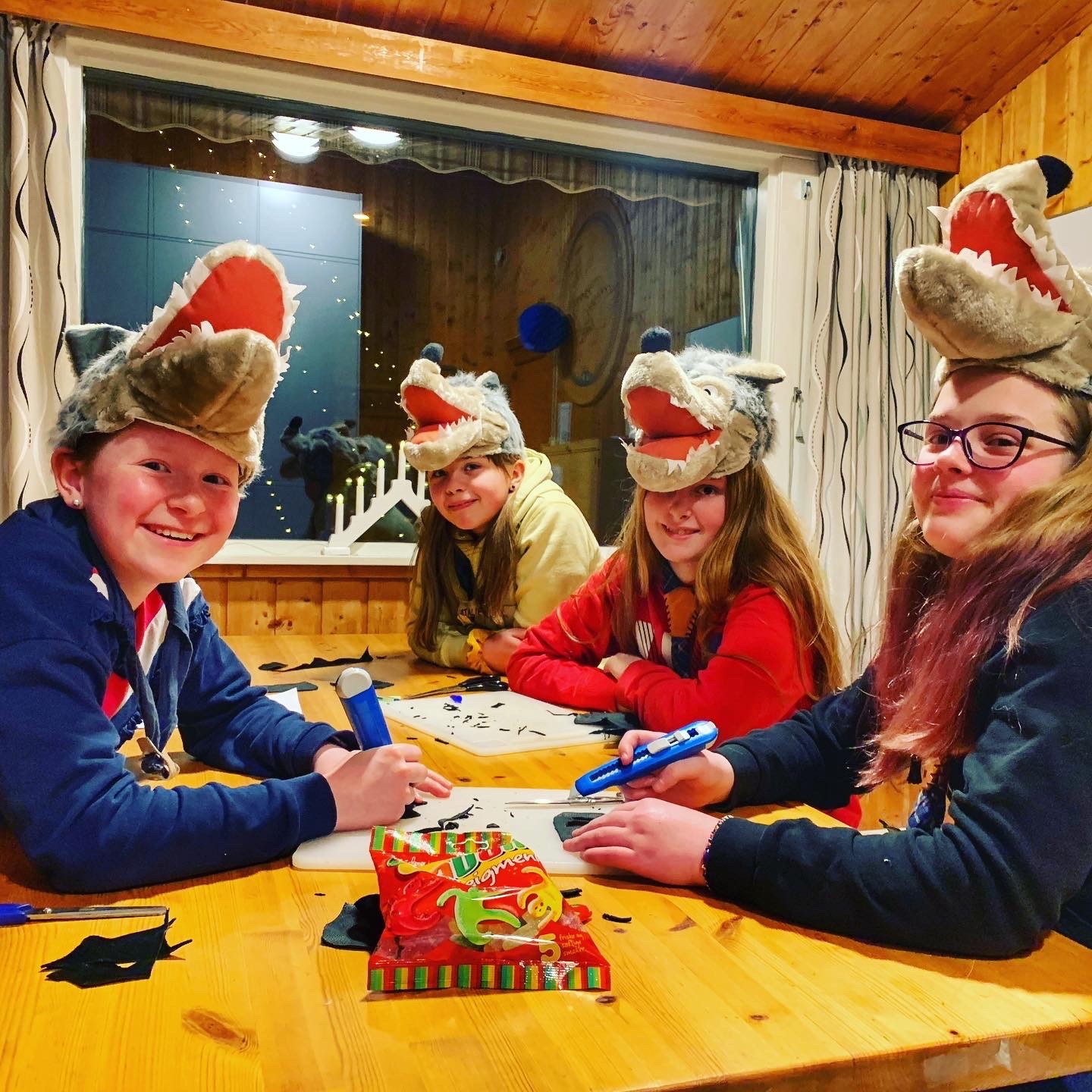 Fire speidere sitter rundt et bord og lager patruljesærpreg, med morsomme ulvehatter på hodet
