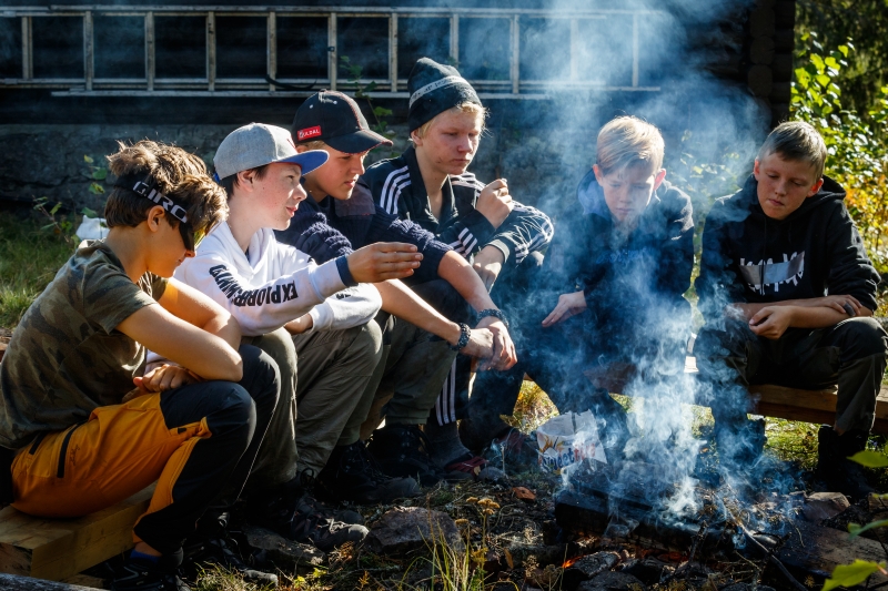 Gruppe ungdommer sitter rundt et lite bål ute i naturen