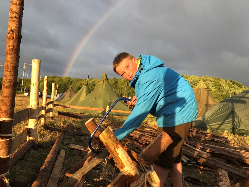 Gutt i blå jakke med en regnbue i bakgrunnen på en leirplass. Foto: Thomas Markento Andresen