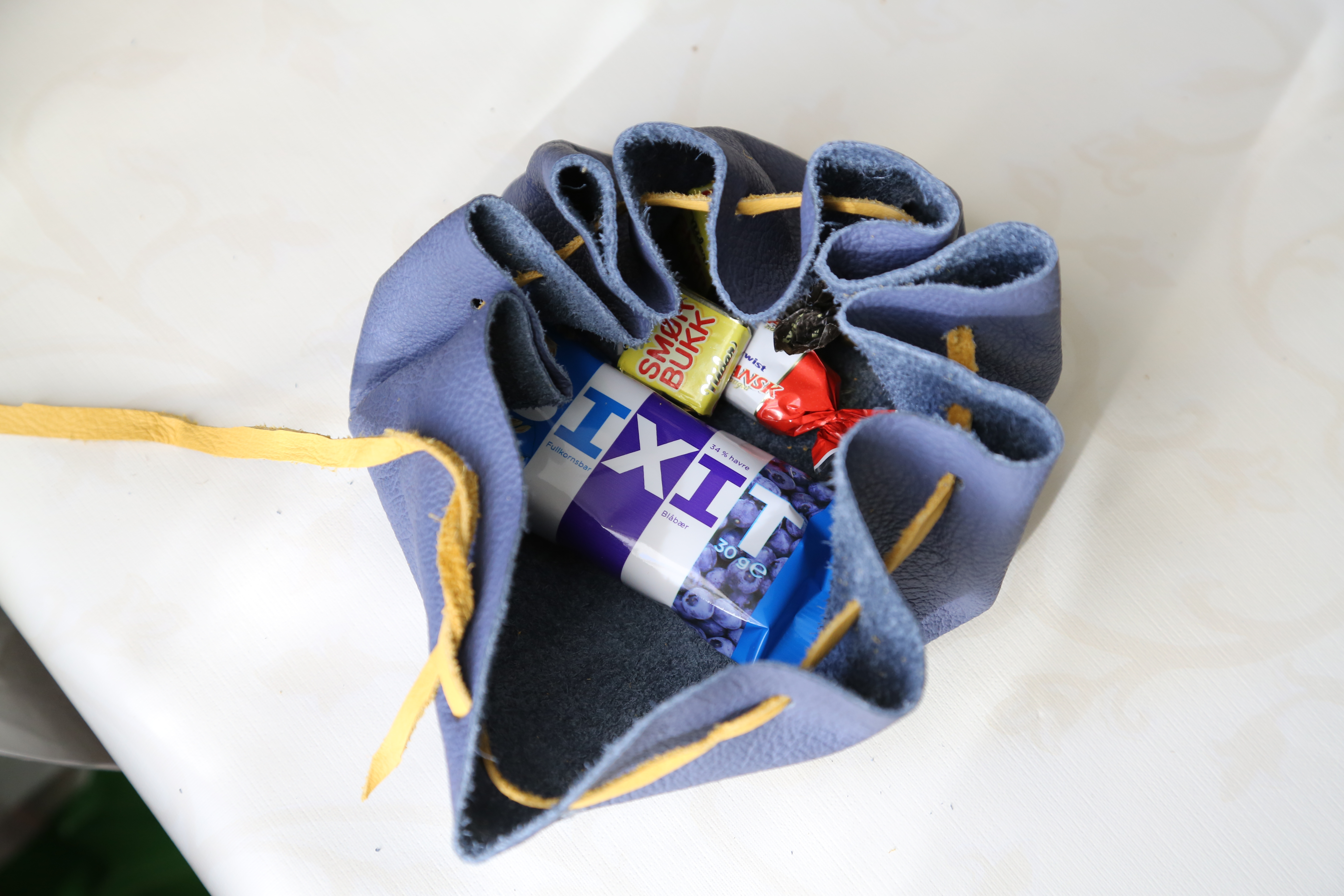 En åpen mulepose av blått skinn med gul skinnsnor, fylt med snacks som bixit-bar og twist